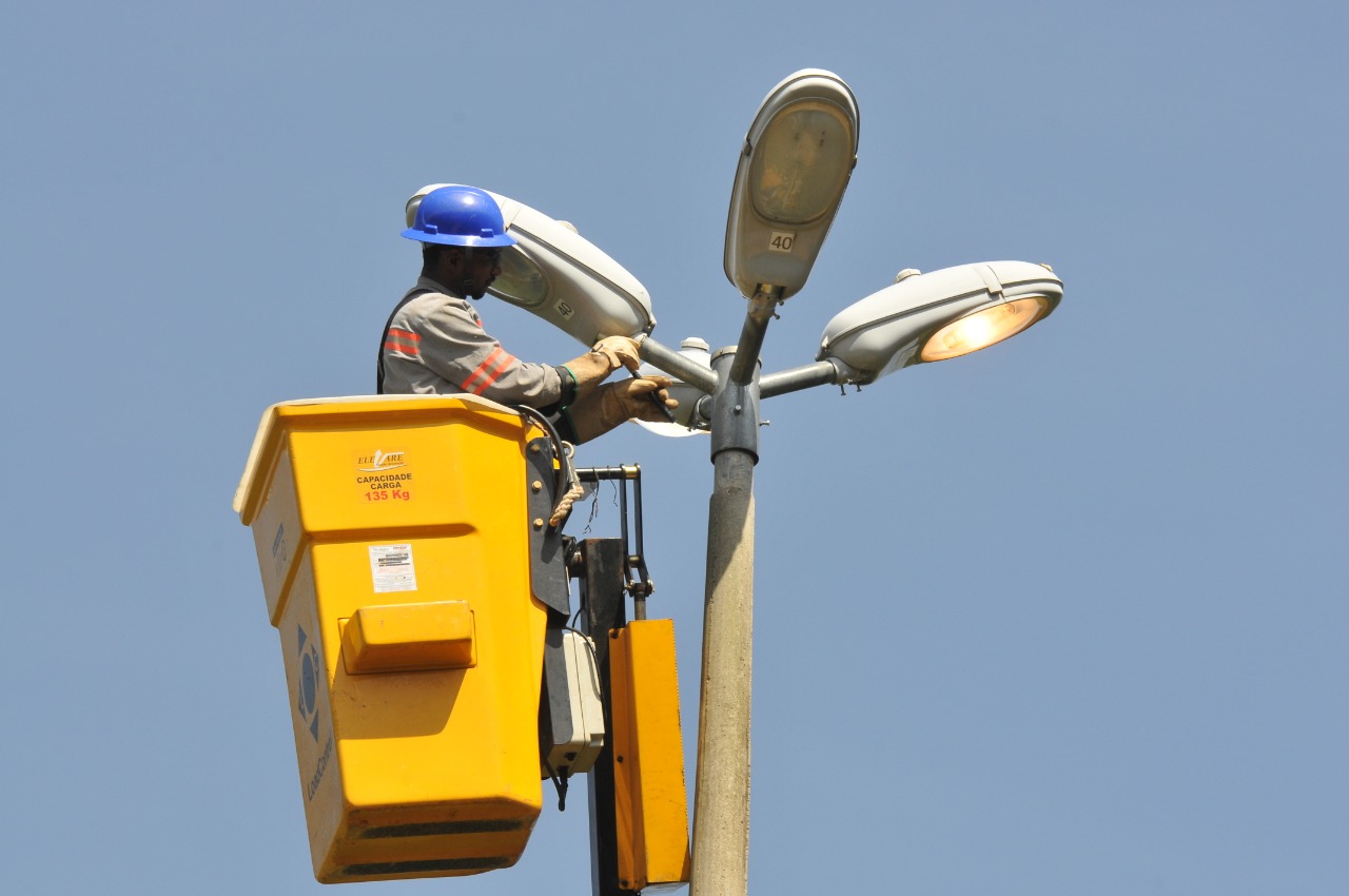 Trabalhador em plataforma elevada faz manutenção em um poste de iluminação pública