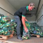 Trabalhador organiza sacos com frutas e verduras dentro de um veículo de entrega