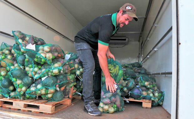 Trabalhador organiza sacos com frutas e verduras dentro de um veículo de entrega