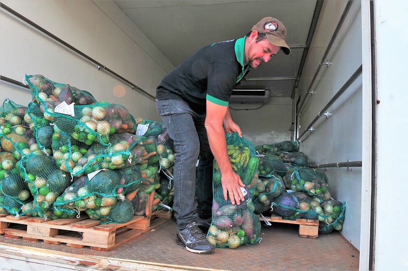 Trabalhador organiza sacos com frutas e verduras dentro de um veículo de entrega