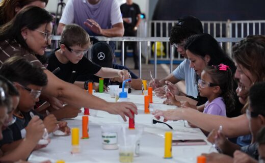 Crianças com óculos de proteção participam de uma experiência científica acompanhadas por adultos