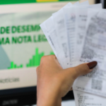 Pessoa segura notas fiscais diante de uma tela do programa Nota Legal