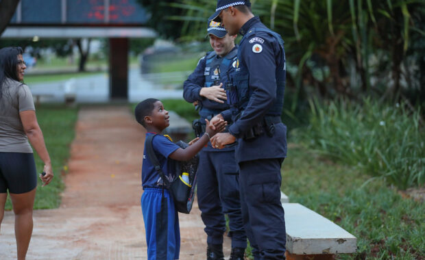 Policiais conversam com um estudante uniformizado próximo a uma escola