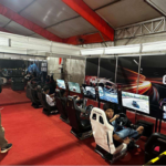 Visitantes usam simuladores de corrida com telas e cadeiras em uma arena de jogos eletrônicos