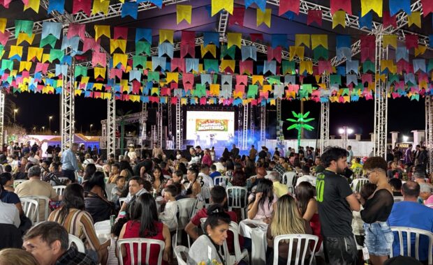 Público participa de festa paroquial com bandeirinhas coloridas, mesas e palco iluminado