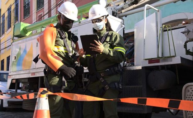 Profissionais com equipamentos de segurança trabalham ao lado de veículo de manutenção elétrica
