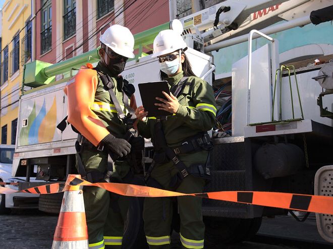 Profissionais com equipamentos de segurança trabalham ao lado de veículo de manutenção elétrica