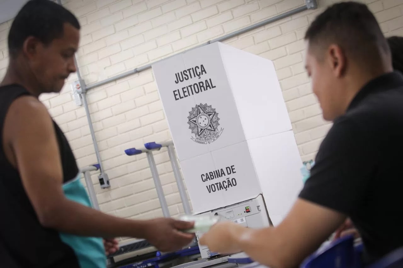 Eleitor entrega documento ao lado de uma cabine de votação