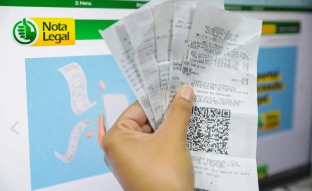 Consumidor segura notas fiscais diante da página do programa Nota Legal