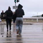 Pedestres atravessam pista molhada durante chuva em Brasília