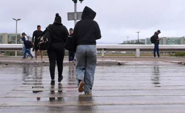 Pedestres atravessam pista molhada durante chuva em Brasília