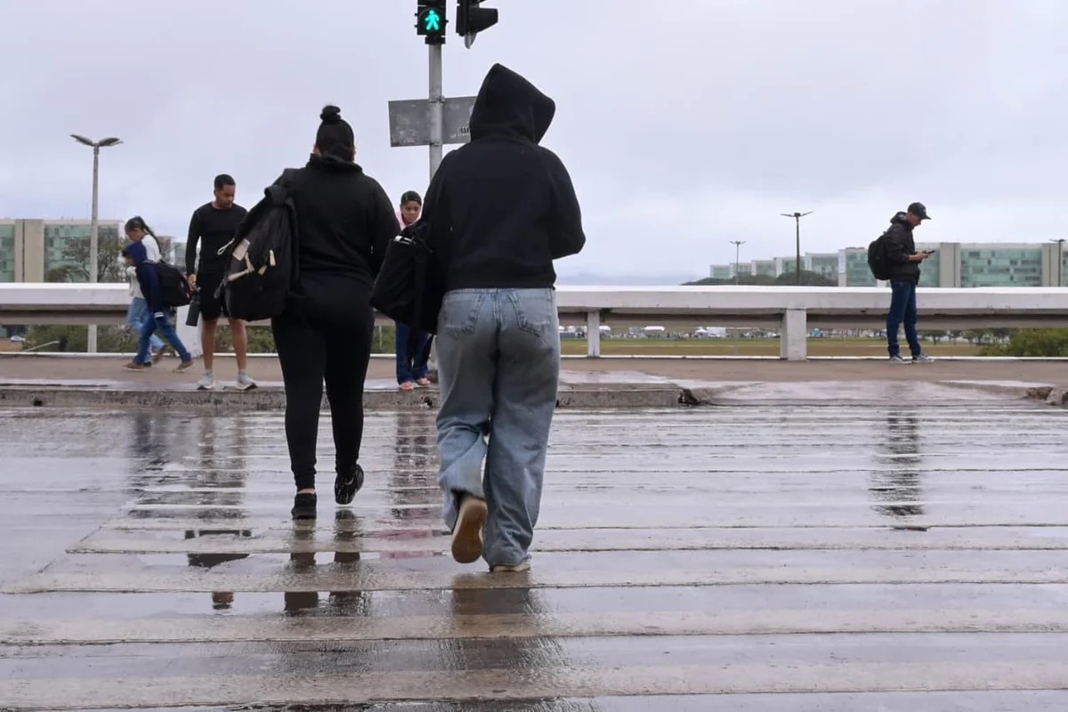 Pedestres atravessam pista molhada durante chuva em Brasília